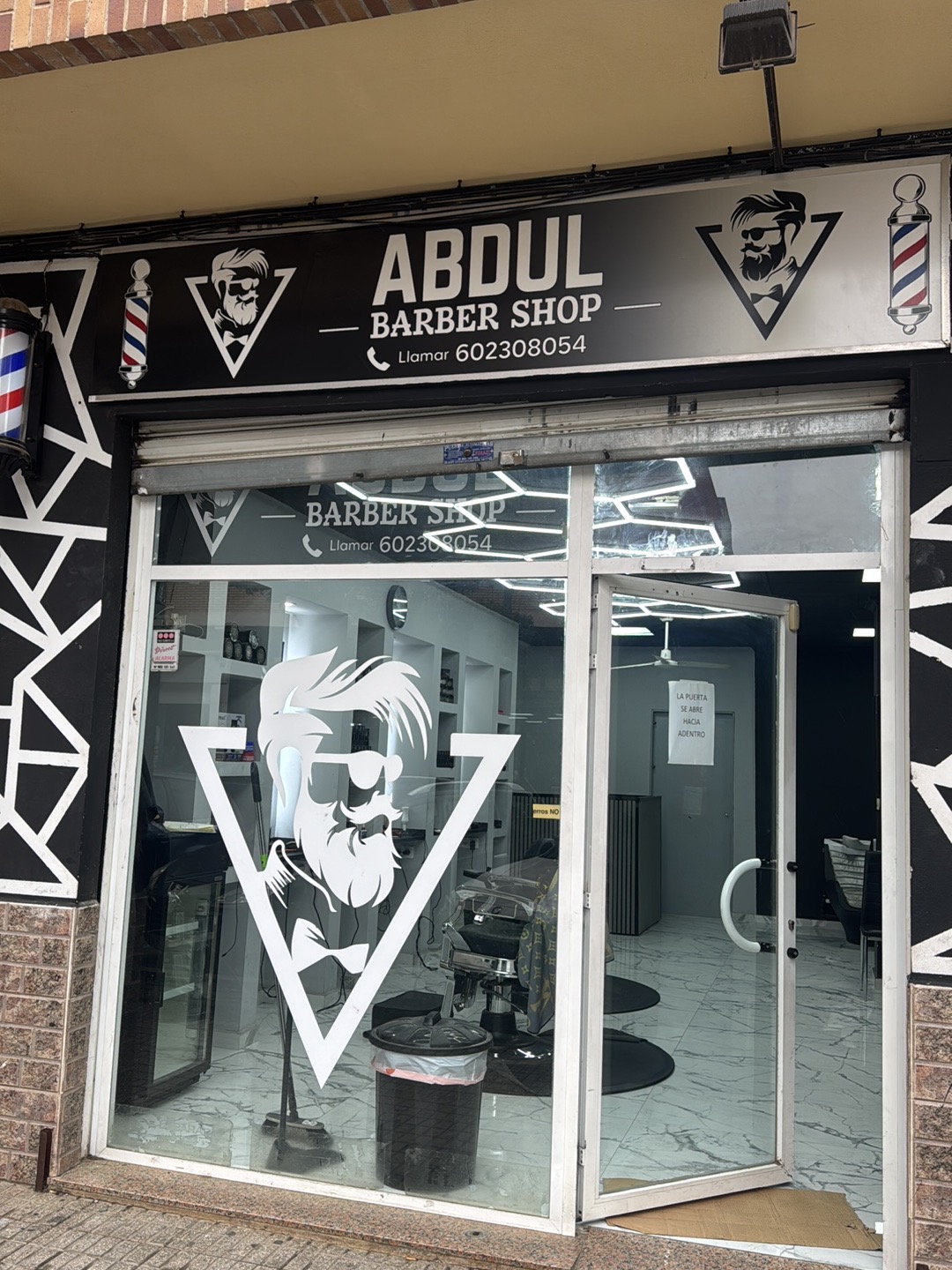 Fachada de Abdul Barber Shop con el rótulo y el dibujo de barbero en el cristal